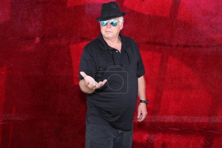 Foto de Un hombre con sombrero negro y gafas de sol mientras posa para que su foto sea tomada mientras está en una cabina de fotos en una fiesta. - Imagen libre de derechos