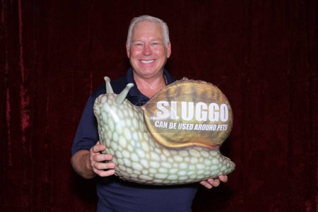 Téléchargez les photos : Un homme sourit alors qu'il tient un très grand escargot gonflable dans une cabine photo - en image libre de droit