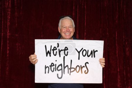 Photo for A man holds a sign which read We are your neighbors while having his pictures taken in a Photo Booth at a Wedding. People love Photo Booths at Weddings and all sorts of Parties and events. - Royalty Free Image