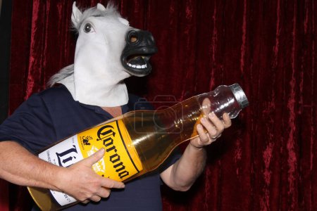 Téléchargez les photos : Lake Forest, Californie - États-Unis - 6 septembre 2023 : Un homme masqué à cheval tient une bouteille de bière Corona gonflable alors qu'il sourit et pose pour que ses photos soient prises dans une cabine photo. - en image libre de droit