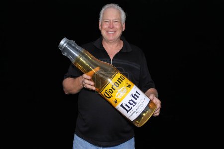 Photo for Lake Forest, California - USA - May 15, 2016: A man holds a Inflatable Corona Beer Bottle while he smiles and poses for his pictures to be taken while in a Photo Booth - Royalty Free Image