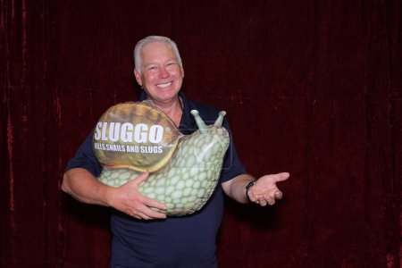 Photo for A man smiles as he holds a Very Large Inflatable Snail while in a Photo Booth - Royalty Free Image
