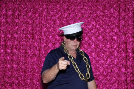 Photo for A man in white cap and sunglasses poses for his picture to be taken while in a Photo Booth at a Party. - Royalty Free Image