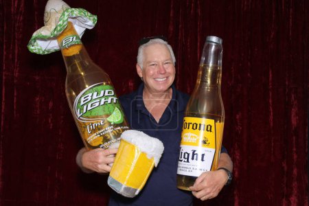 Photo for Lake Forest, California, USA - May 15, 2016: A man holds a Inflatable Corona Beer Bottle while he smiles and poses for his pictures to be taken while in a Photo Booth. - Royalty Free Image
