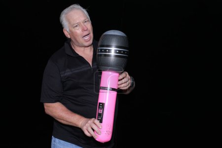 Téléchargez les photos : Bel homme d'âge moyen posant avec un grand microphone gonflable pour sa photo à prendre dans un photomaton lors d'une fête - en image libre de droit