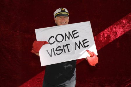 Photo for A man smiles and holds a COME VISIT ME Sign while waiting for his pictures to be taken in a Photo Booth. - Royalty Free Image
