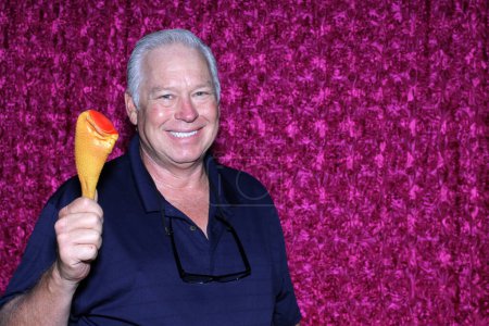 Foto de Un hombre sonríe mientras muestra su pierna de pollo de plástico mientras se toma una foto en una cabina de fotos - Imagen libre de derechos