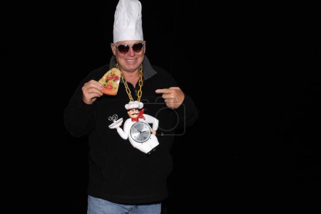 Photo for A man wears a Chef Hat and a Chef Clock Necklace while waiting for his pictures to be taken in a Photo Booth. Everyone loves a Photo Booth even Chefs and Fast Food Cook - Royalty Free Image