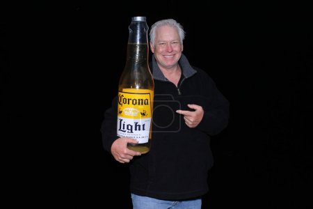 Photo for Lake Forest, California - USA - May 15, 2016: A man holds a Inflatable Corona Beer Bottle while he smiles and poses for his pictures to be taken while in a Photo Booth - Royalty Free Image