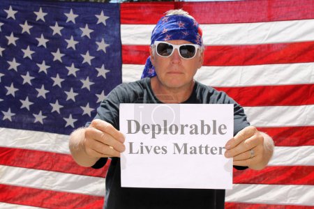 Téléchargez les photos : Un homme pose devant un drapeau américain avec un signe déplorable Lives Matter. - en image libre de droit