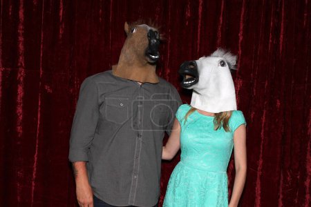 Unidentifiable People wear Horse Head Masks and pose and play while their pictures are taken in a Photo Booth