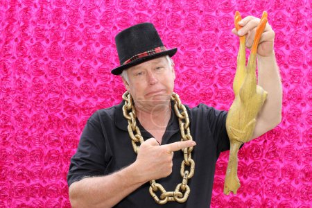 Photo for A man is sad and frowns as he holds up a dead rubber chicken while he has his picture taken in a Photo Booth. Photo Booths are fun at all parties and events. Rubber Chickens Love Photos. - Royalty Free Image