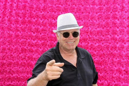 Foto de Guapo hombre de mediana edad en sombrero blanco posando para que su foto sea tomada mientras está en una cabina de fotos en una fiesta - Imagen libre de derechos