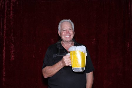 Foto de El hombre sonríe mientras disfruta de una taza gigante de cerveza mientras toma sus fotos en una cabina de fotos en una fiesta. - Imagen libre de derechos
