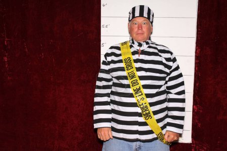 Photo for Photo Booth. A man wears a Prison Striped Uniform in front of a Police Mugshot Chart aka booking photograph. - Royalty Free Image