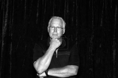 Téléchargez les photos : Photo en noir et blanc d'un bel homme d'âge moyen posant pour que sa photo soit prise dans un photomaton lors d'une fête - en image libre de droit