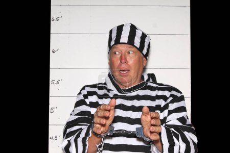 Téléchargez les photos : Photo Booth. Un homme porte un uniforme rayé en prison devant un Mugshot Chart de la police aka photo de réservation. - en image libre de droit