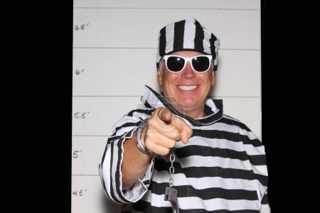Téléchargez les photos : Photo Booth. Un homme porte un uniforme rayé en prison devant un Mugshot Chart de la police aka photo de réservation. - en image libre de droit