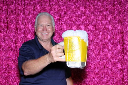 Foto de El hombre sonríe mientras disfruta de una taza gigante de cerveza mientras toma sus fotos en una cabina de fotos en una fiesta. - Imagen libre de derechos