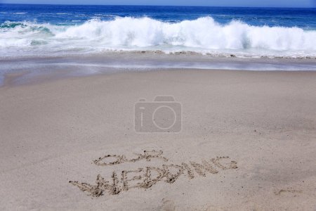 Foto de Palabras Nuestra boda escrita en la arena en la playa con la marea oceánica y las olas del océano - Imagen libre de derechos