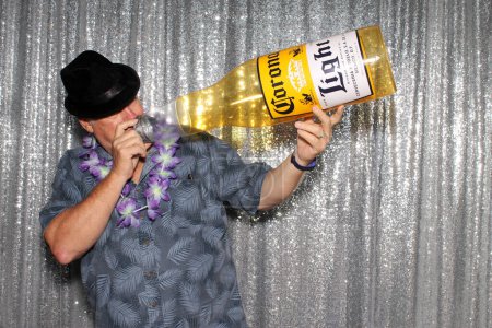 Foto de Lake Forest, California - Estados Unidos - 15 de mayo de 2016: Un hombre sostiene una botella inflable de cerveza Corona mientras sonríe y posa para que sus fotos sean tomadas mientras está en una cabina de fotos - Imagen libre de derechos