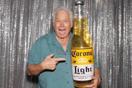 Foto de Lake Forest, California - Estados Unidos - 11 de septiembre de 2023: Un hombre sostiene una botella inflable de cerveza Corona mientras sonríe y posa para que sus fotos sean tomadas mientras está en una cabina de fotos. Las cabinas de fotos son divertidas. - Imagen libre de derechos