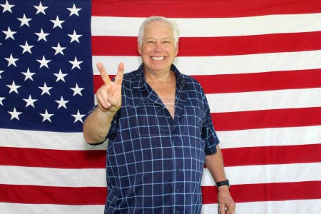 Foto de Un hombre americano orgulloso saluda y posa delante de la bandera americana mientras espera que sus fotos sean tomadas mientras está en una cabina de fotos en una fiesta del 4 de julio. - Imagen libre de derechos