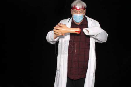 Téléchargez les photos : Un docteur est choqué quand il découvre que sa main gauche s'est séparée de son bras avec un fond noir. Méfiez-vous de la mauvaise médecine. Costume d'Halloween. Kiosque photo Halloween. Urgence médicale - en image libre de droit