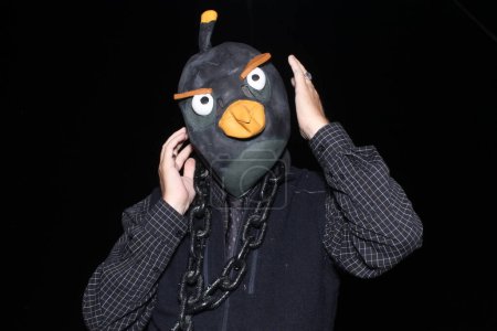 Foto de Un hombre lleva una máscara de cabeza de pájaro mientras toma sus fotos en una cabina de fotos en una fiesta de Halloween. Halloween es el momento perfecto para una fiesta de cabina de fotos. - Imagen libre de derechos