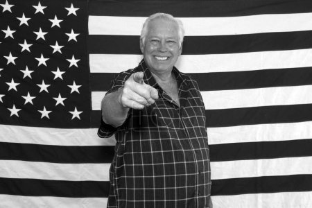 Photo for A proud American Man points at camera and Poses in front of the American Flag while waiting for his pictures to be taken while in a photo booth at a Fourth of July Party. - Royalty Free Image