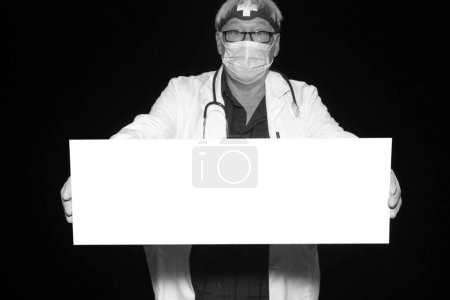 Téléchargez les photos : Un médecin tient une pancarte blanche vierge avec de la place pour votre message, publicité ou images tout en faisant prendre ses photos dans une cabine photo lors d'un congrès médical. - en image libre de droit