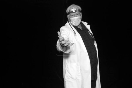 Téléchargez les photos : Un docteur maléfique pose alors qu'il se fait prendre en photo dans une cabine photo d'Halloween avec des rideaux de velours noir. Méfiez-vous de la mauvaise médecine. Photo noir et blanc - en image libre de droit