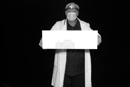 Téléchargez les photos : Un médecin tient une pancarte blanche vierge avec de la place pour votre message, publicité ou images tout en faisant prendre ses photos dans une cabine photo lors d'un congrès médical. - en image libre de droit