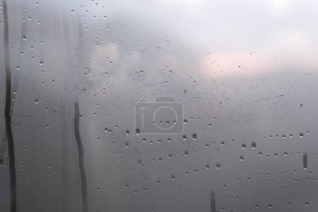 Téléchargez les photos : Vue sur la ville par une fenêtre un jour pluvieux. La pluie tombe sur la vitre. - en image libre de droit