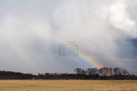 Téléchargez les photos : Un arc-en-ciel se forme derrière une tempête qui passe avec un champ de ferme au premier plan. - en image libre de droit