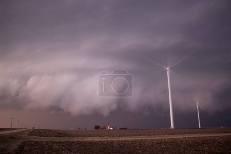 Wind turbines spin rapidly as a large storm cloud approaches in the rural countryside.