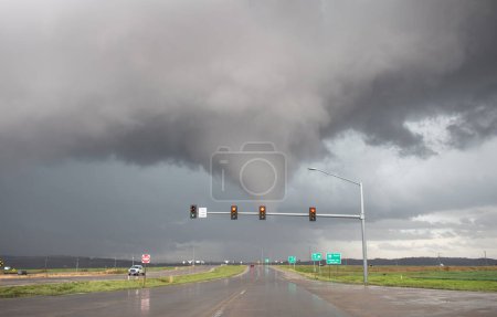 A tornado crosses the road up ahead beyond a traffic light. The pavement is still wet from the passing storm.