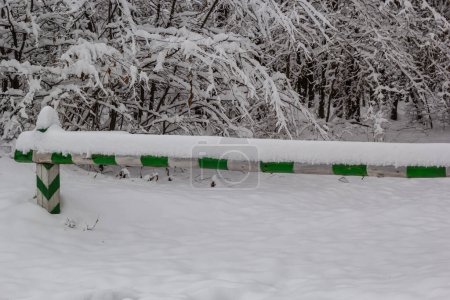 Foto de Green and white barrier preventing passage into the forest. Covered with white snow on a cloudy winter day. - Imagen libre de derechos