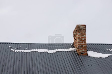 Photo for A brick chimney on a metal roof in the winter under the snow. construction concept. - Royalty Free Image