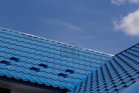 Das Dach eines Hauses, das an einem Sommertag vor dem Hintergrund des Himmels mit blauen Metallziegeln bedeckt ist. Geschäft, das Baumaterialien verkauft oder Hausdächer repariert.