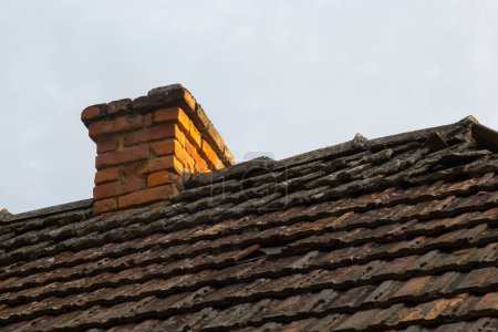 Téléchargez les photos : Cheminée en brique rouge au sommet de la maison de village. Un toit en tuiles sur le fond du ciel. - en image libre de droit
