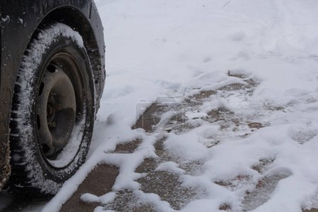 Verkehr auf winterlichen Straßen nach starkem Schneefall. Nahaufnahme von Winterreifen am Auto auf schneeglatter Straße in der Stadt.