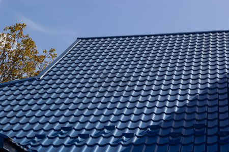 The roof of a house covered with sheets of blue metal tiles against the background of the sky on a summer day. Business selling building materials or repairing house roofs.