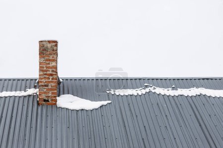 Photo for A brick chimney on a metal roof in the winter under the snow. construction concept. - Royalty Free Image