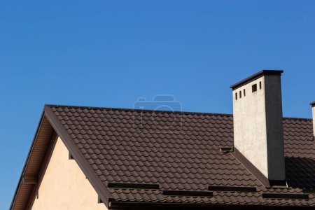 Rotes Hausdach mit rotem Ziegelkamin. Keramischer Schornstein, Dachziegel aus Metall, Dachrinnen.