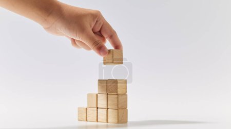 Photo for Close-up hand putting wood cubes stacked as stair step shapes mock-up for creating symbols or logos, business growth, and management concept on white background - Royalty Free Image