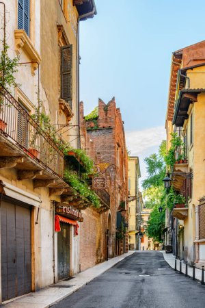 Foto de Verona, Italia - 24 de agosto de 2014: Vista de la calle estrecha en el centro histórico de Verona, Italia. Fachadas de casas al sol de la mañana. Verona es un destino turístico popular de Europa. - Imagen libre de derechos