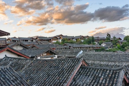 Traditional Chinese black tile roofs of authentic houses in the Old Town of Lijiang, China. Awesome view of colorful sunset sky. Lijiang is a popular tourist destination of Asia.