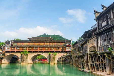 Photo for The Hong Bridge (Rainbow Bridge) over the Tuojiang River (Tuo Jiang River) and old authentic traditional Chinese wooden riverside houses on stilts in Phoenix Ancient Town (Fenghuang County), China. - Royalty Free Image