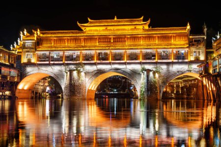 Photo for Colorful night view of the Hong Bridge (Rainbow Bridge) over the Tuojiang River (Tuo Jiang River) in Phoenix Ancient Town (Fenghuang County), China. Fenghuang is a popular tourist destination of Asia. - Royalty Free Image